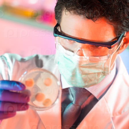 Mask protected life science professional observing the petri dish. Focus on scientist\'s eye.