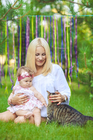 Young mother with child and a cat having fun on green lawn on summer day