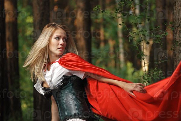 Portrait of a blonde lady in old-fashioned dress and red cloak in a fairy forest