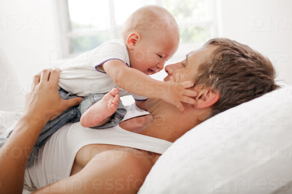 Young smiling father with his nine months old son on the bed at home on white home background, stock photo