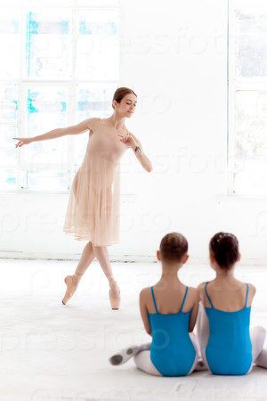 Two little ballerinas dancing with personal ballet teacher in dance studio