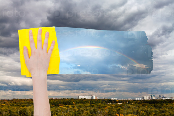 hand deletes gray clouds over city by yellow cloth