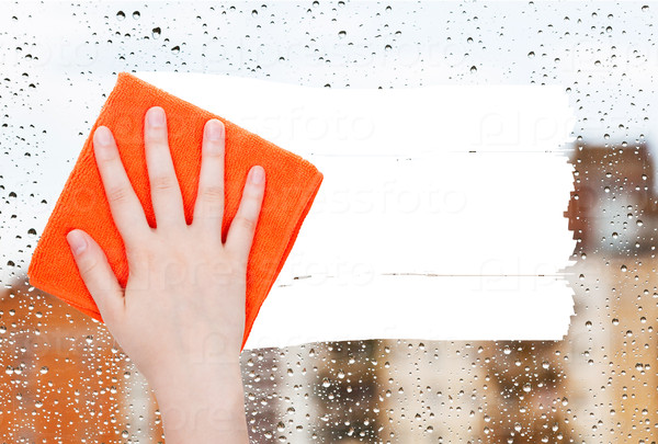 weather concept - hand deletes rain drops on window by orange rag from image and white empty copy space are appearing