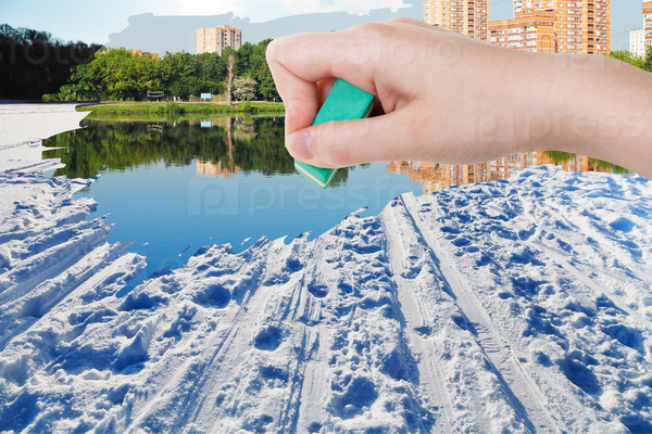 weather concept - hand deletes winter snow field by rubber eraser from image and summer cityscape are appearing