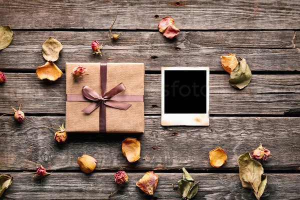 Blank photo frame with gift box, petals and rose flowers on old wooden background.
