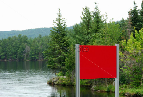 Red sign on waterfront in front of forest