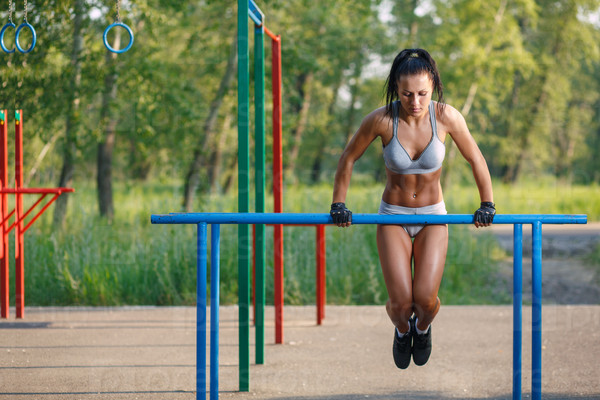 beautiful fitness woman doing exercise on parallel bars sunny outdoor. Sporty girl doing push ups on bars outdoor