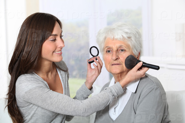 Young woman helping old woman to put makeup on