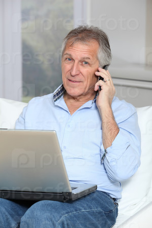 Senior man in sofa with laptop computer and mobile phone