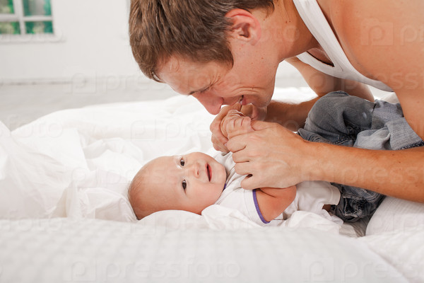 Young smiling father with his nine months old son on the bed at home on white home background