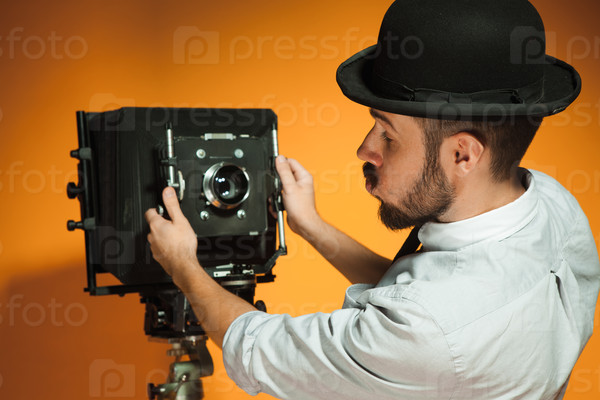 back view of young man in hat as photographer with retro camera on an orange background
