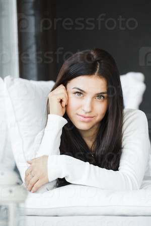 portrait of a young beautiful woman smiling with her crossed arms on the bed, her legs raised and crossed.