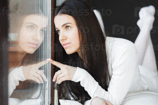 portrait of a Young beautiful woman sitting on couch at her room near window in white
