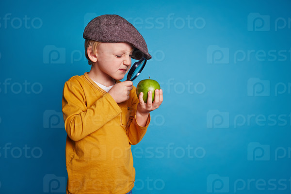 Little boy looking at green apple through magnifying glass, stock photo