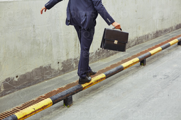 Rear view of businessman with briefcase balancing on yellow-and-black road curb
