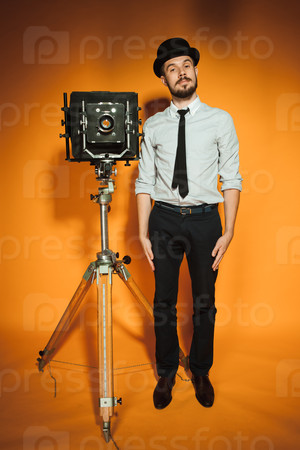 Young man in hat as photographer with retro camera on an orange background