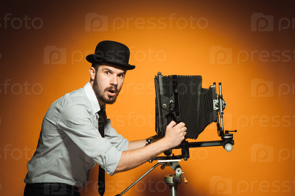 side view of young  afraid man in hat as photographer with retro camera on an orange background