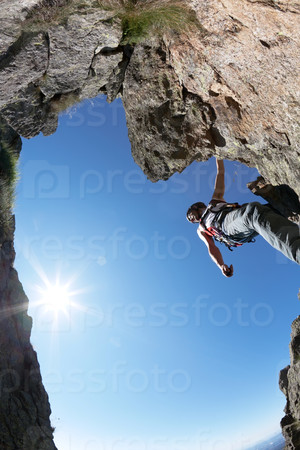 Terrific view of a climbing route: young man climbing a rocky ridge, back-light, fish-eye lens, vertical frame.