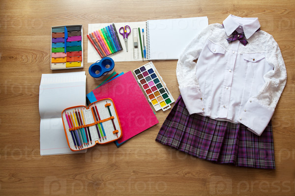 set of school supplies. red skirt, white blouse, pen, pencil, clored paper, copybook, watercolor paint on the floor