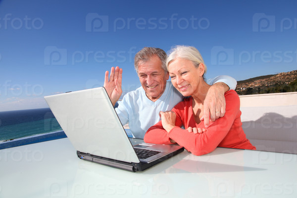 Senior couple waving at webcamera on laptop computer