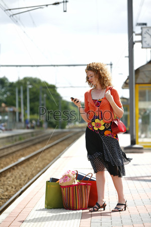 Young woman holding a mobile phone while waiting for a train at the platform with a lot of bags