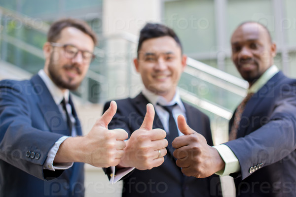 Close-up of multi ethnic business team holding their thumbs up. Three  men hands showing thumbs up against the backdrop of the city. The one man is European, other is Chinese and African-American.