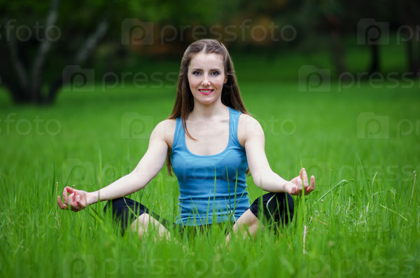 Young girl practicing yoga in nature in the woods on a background of green trees and grass.