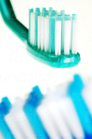 Closeup of two toothbrushes: the first one in focus, the other one out of focus, isolated against white