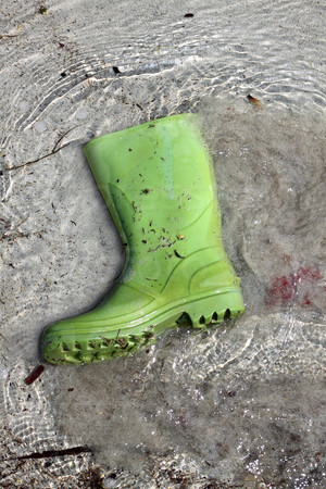 green boots trash on beach shore pollution human waste concept