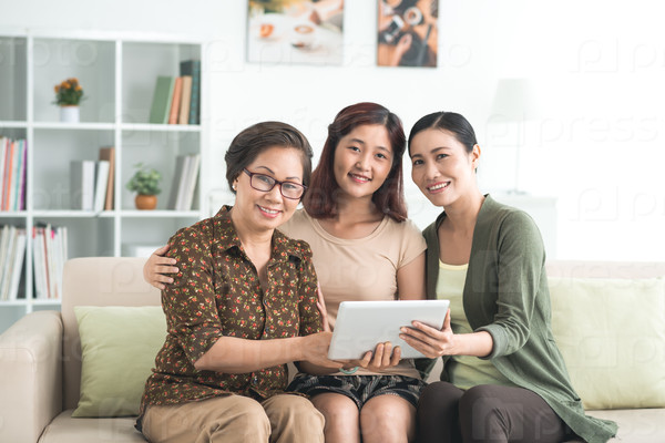 Smiling Vietnamese family of three using digital tablet at home