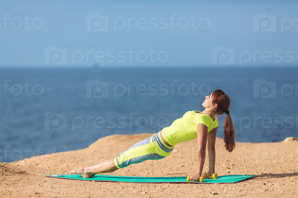 Woman training with dumbbells on the beach. Summer work out, fitness and exercising with weights outdoor. Caucasian sport girl training hard.