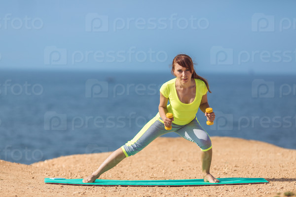 Woman training with dumbbells on the beach. Summer work out, fitness and exercising with weights outdoor. Caucasian sport girl training hard.