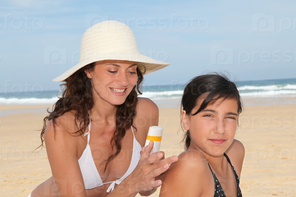 Mother spreading sunscreen on her daughter\'s shoulders