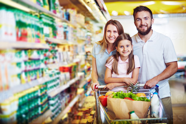 Joyful family of father, mother and daughter looking at camera in supermarket