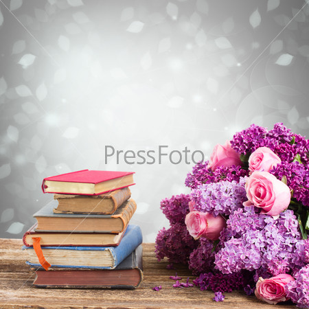 pile of books with lilac and rose flowers on gray bokeh  background