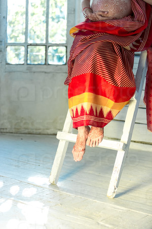 Indian picture on woman feet, mehendi tradition decoration, resistant design by special paint, brown henna. Woman sitting in indian red dress on white wooden staircase background