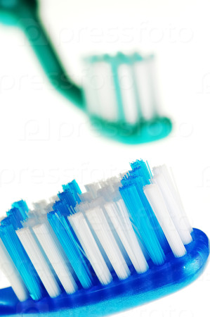 Closeup of two toothbrushes: the first one in focus, the other one out of focus, isolated against white