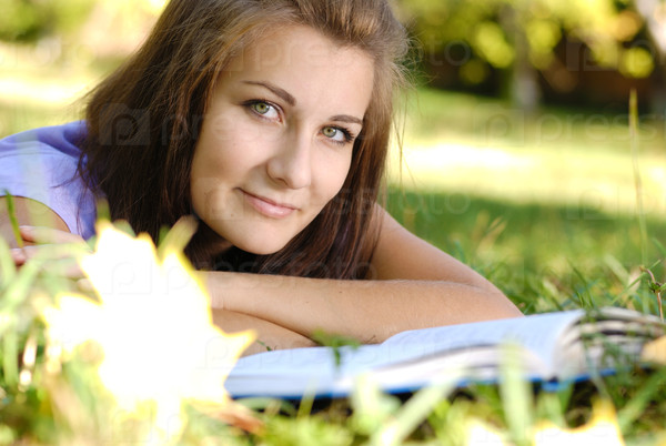 Beautiful brunette long haired girl takes rest with book outdoors