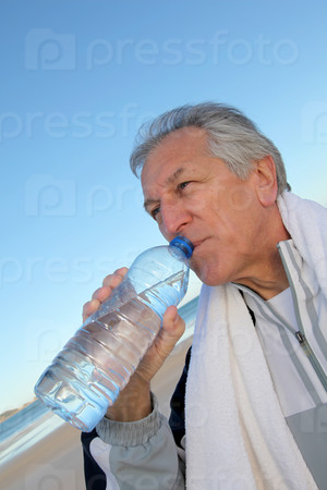 Active senior drinking water from bottle at the beach