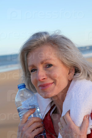 Active senior woman drinking water from bottle at the beach