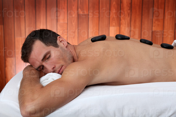 Man relaxing on massage bed with hot stones