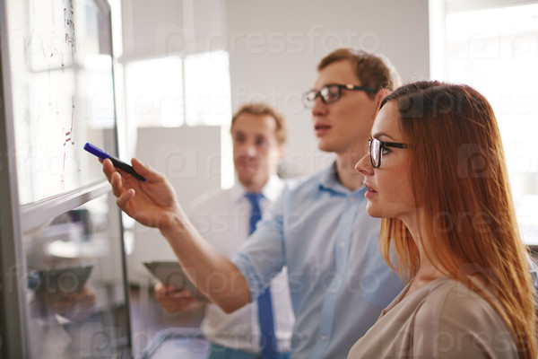 Serious businesswoman looking at information on board while listening to colleague explanations