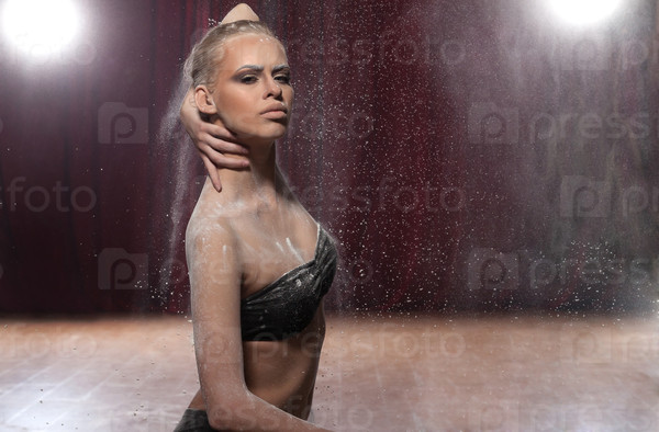 Very attractive young woman in a fashion pose sitting next to a powder smashing background.