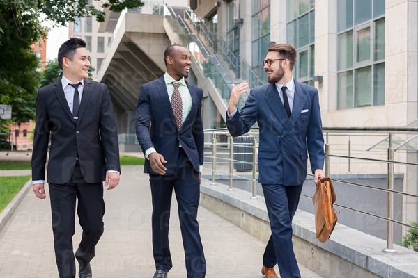 Portrait of multi ethnic business team.Three smiling men walking against the background of city. The one man is European, other is Chinese and African-American.