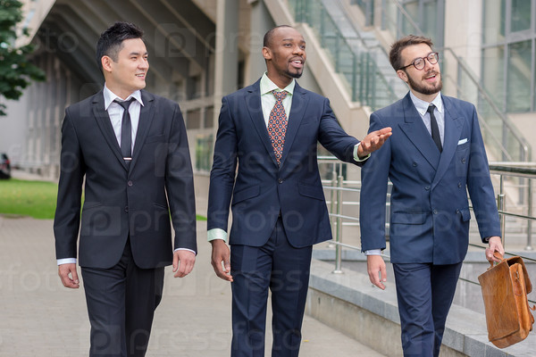 Portrait of multi ethnic business team.Three smiling men walking against the background of city. The one man is European, other is Chinese and African-American.