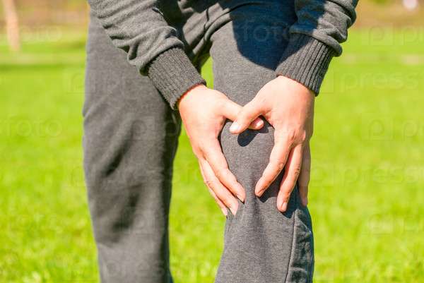 Male hands clasped sore knee outdoors, stock photo