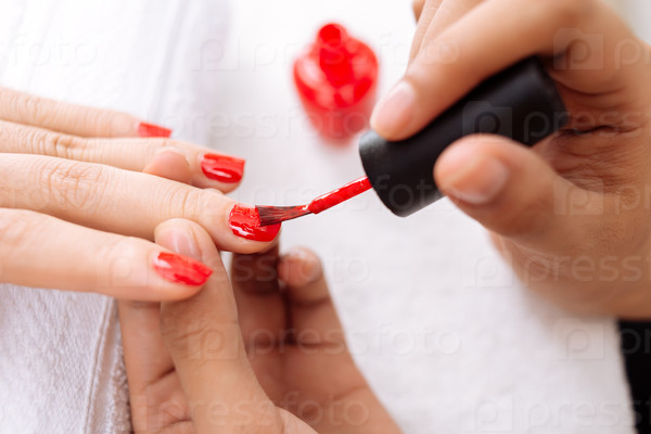 Close-up image of master applying bright red nail polish