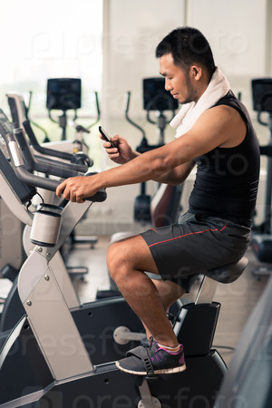Sporty man reading text message on the phone while training on stationary bike