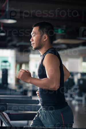 Side view of Vietnamese man running on the treadmill in the gym