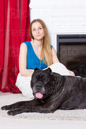 Girl in blue dress sitting by the fireplace with a dog Cane Corso